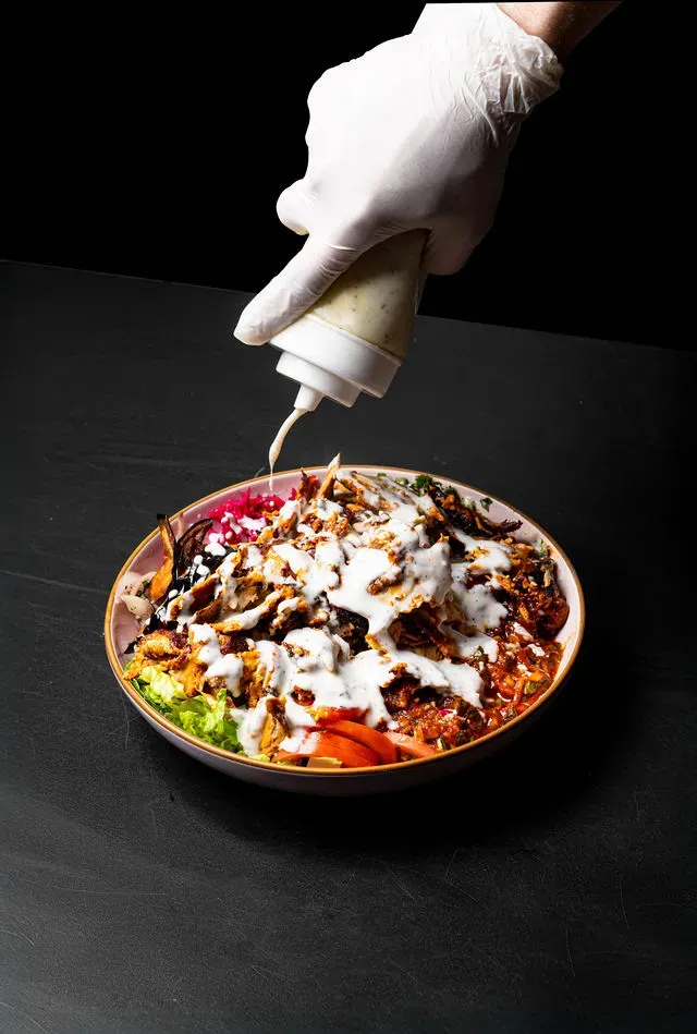 Chicken shawarma bowl with red cabbage and salad drizzled with garlic sauce on dark background