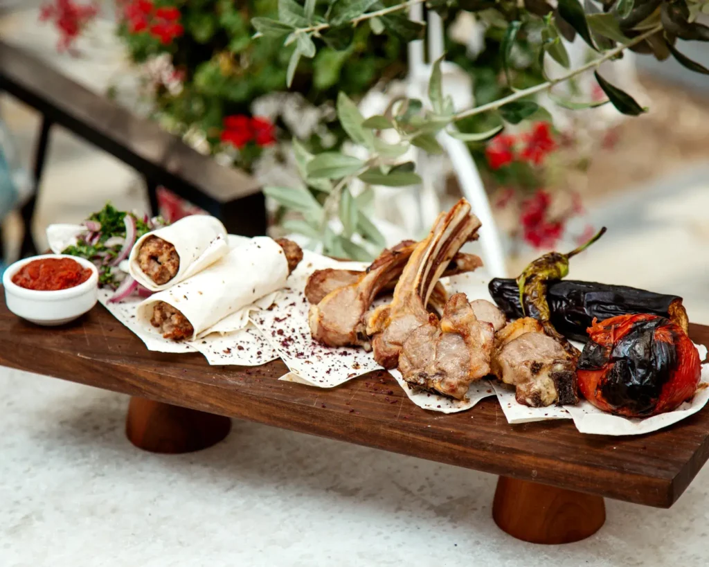 Grilled lamb chops with kofta lavash wraps, roasted vegetables and dipping sauce on a wooden board