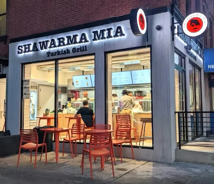 Shawarma Mia Turkish Grill storefront at night with lit signage, customers ordering and patio seating