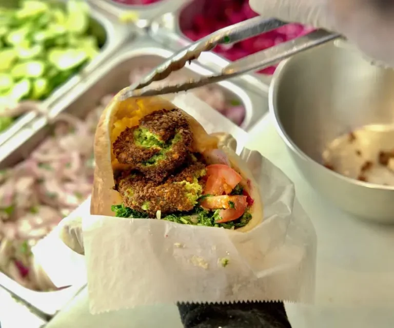Falafel pita stuffed with parsley, tomato and greens held with tongs at the salad bar