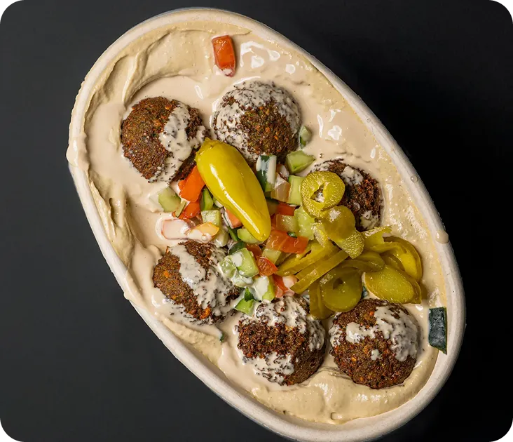 A bowl of falafel balls with hummus, pickles, and diced vegetables.