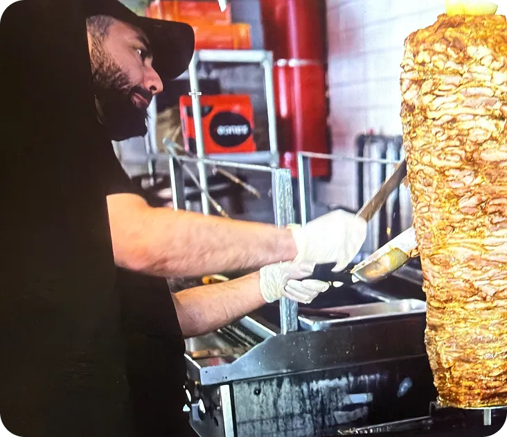 Chef carving chicken shawarma from the vertical rotisserie with a long knife