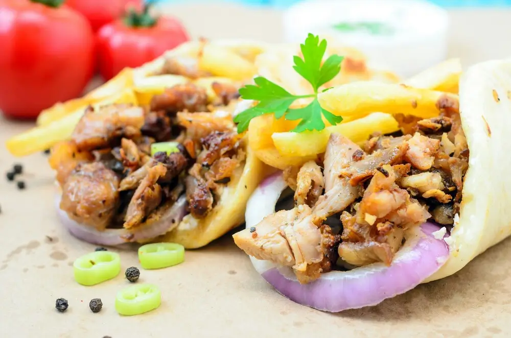 Chicken shawarma wraps with fries, red onion and parsley on flatbread with fresh tomatoes