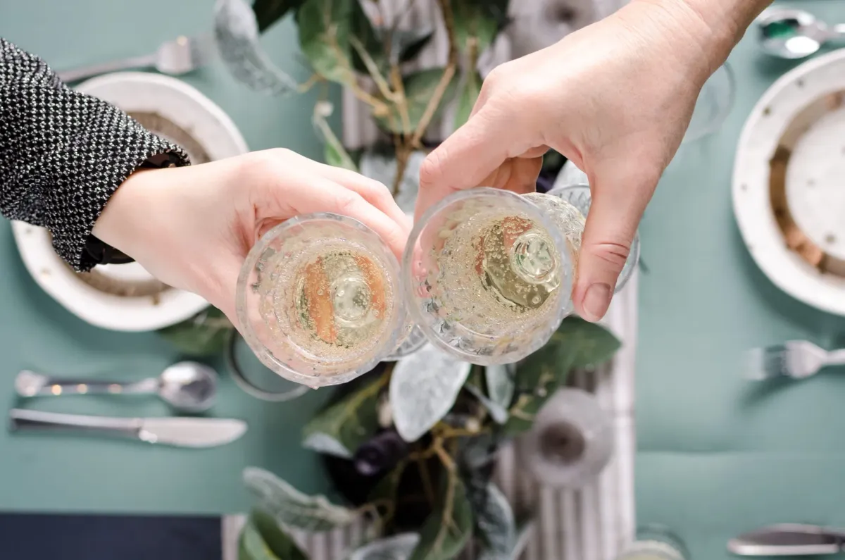 Two hands toasting sparkling wine glasses over a set table