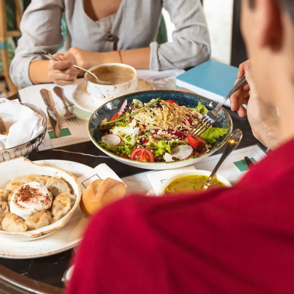 Two people dining over a mixed salad, dumplings with yogurt, soup, and coffee