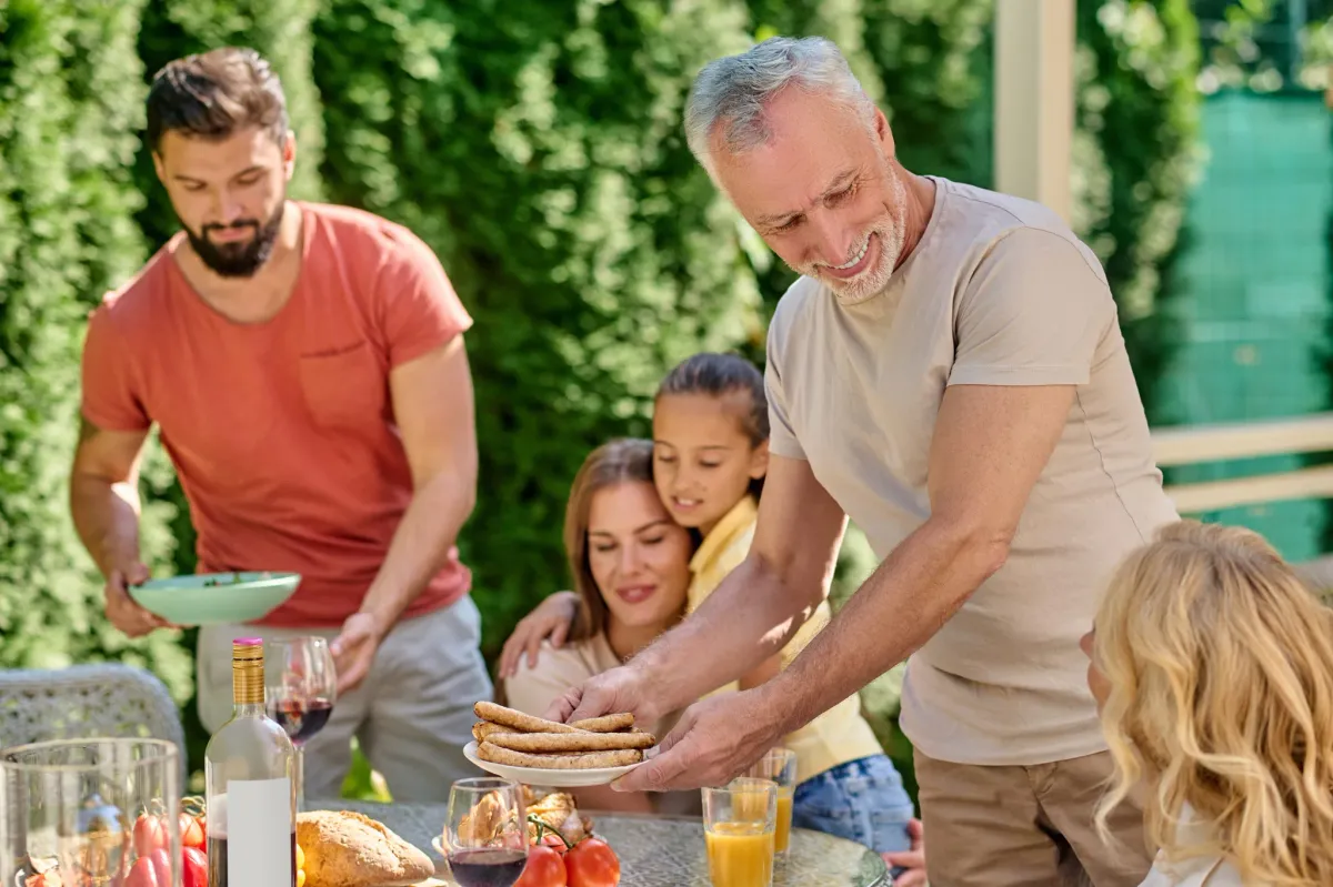 Family sharing an outdoor meal as a man serves grilled kofta to the table