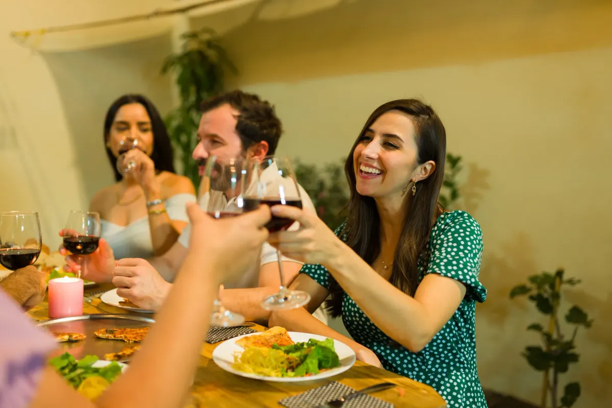 Friends toasting red wine and laughing over dinner at a restaurant table