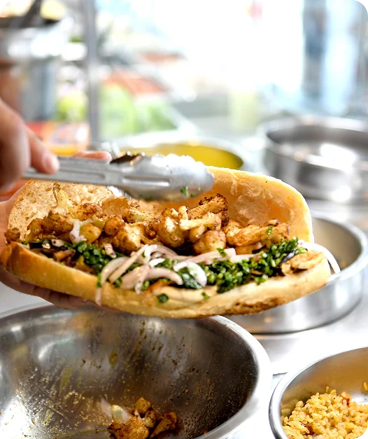 Cook filling a shawarma sandwich with chicken, parsley, and onion at the counter