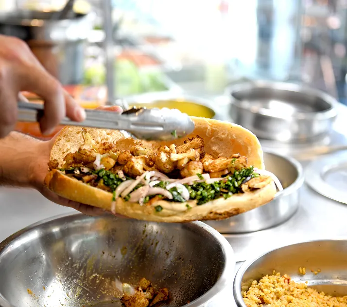 Chicken shawarma sandwich on baguette with parsley, onions and garlic sauce held with tongs