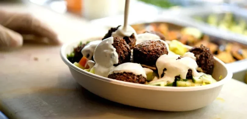 Tahini being drizzled over a falafel bowl with cucumber and chopped salad
