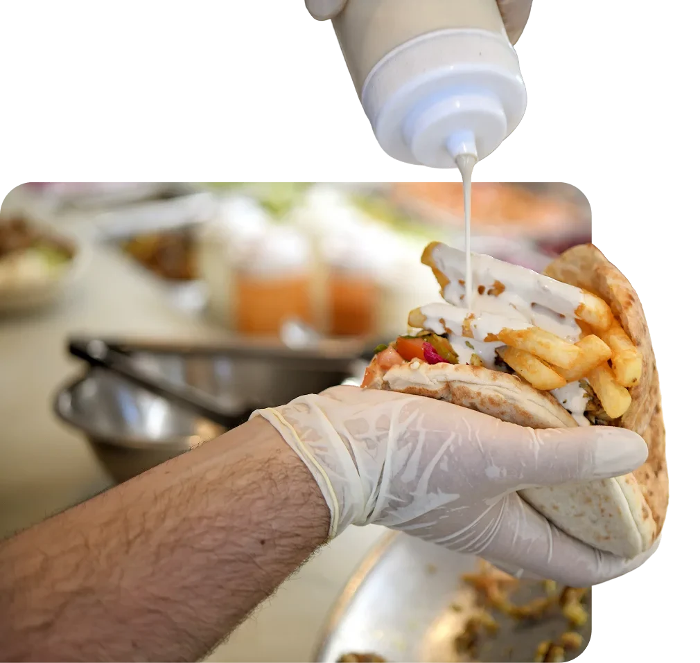Cook adding garlic sauce to a shawarma wrap loaded with fries and meat